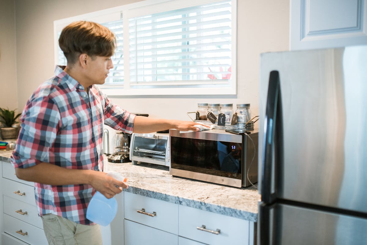 A man wiping a microwave oven in a kitchen